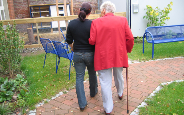 Older person walking with a cane being helped by a younger person